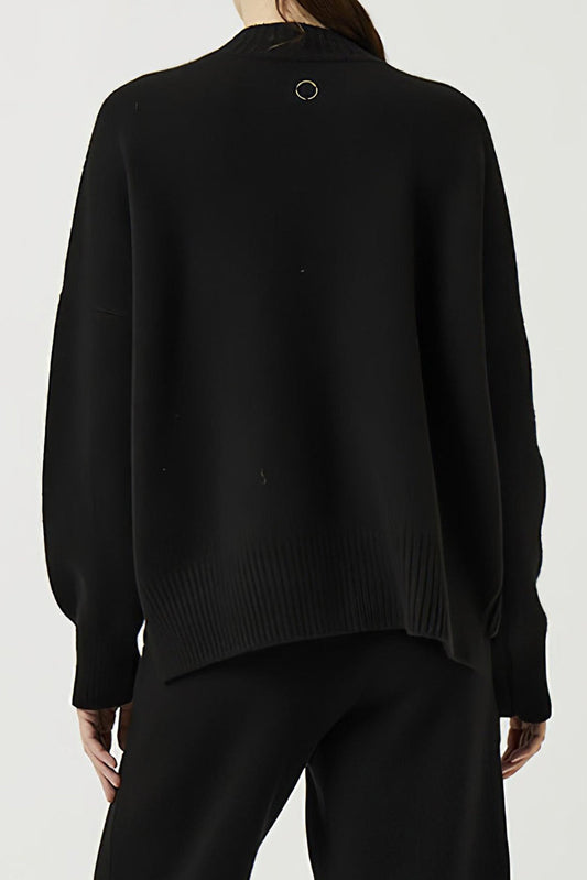 This image features the Aire Cardigan, a luxurious, chunky open cardigan made from pure cashmere. The cardigan is displayed on a model, showcasing its sleek black color and stylish design elements.