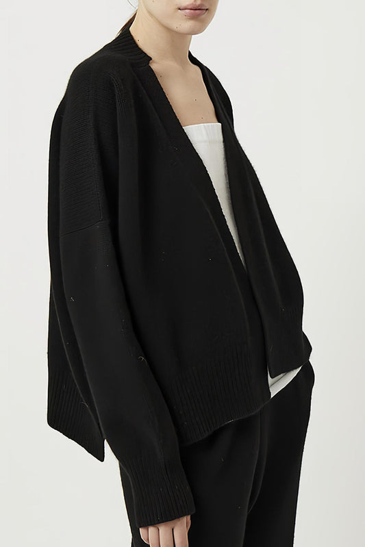 This image features the Aire Cardigan, a luxurious, chunky open cardigan made from pure cashmere. The cardigan is displayed on a model, showcasing its sleek black color and stylish design elements.