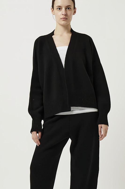 This image features the Aire Cardigan, a luxurious, chunky open cardigan made from pure cashmere. The cardigan is displayed on a model, showcasing its sleek black color and stylish design elements.
