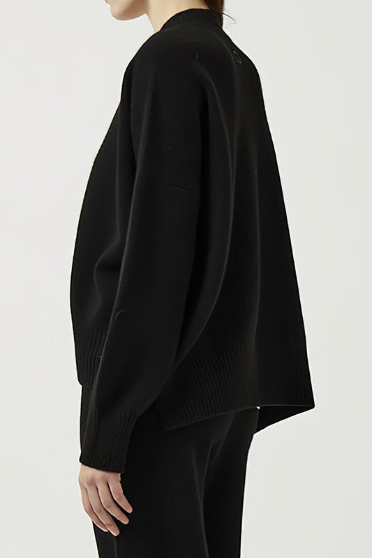 This image features the Aire Cardigan, a luxurious, chunky open cardigan made from pure cashmere. The cardigan is displayed on a model, showcasing its sleek black color and stylish design elements.