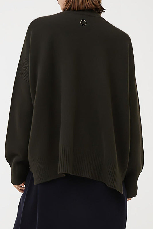 This image features the Aire Cardigan, a luxurious, chunky open cardigan made from pure cashmere. The cardigan is displayed on a model, showcasing its sleek forest color and stylish design elements.