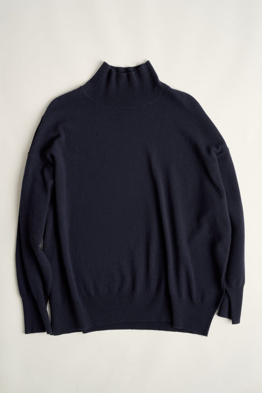 This image features the Kotto Sweater, highlighting its high-neck design and snug, comfortable fit. The sweater is presented in a classic, versatile ocean color, which enhances its elegant and timeless appeal.