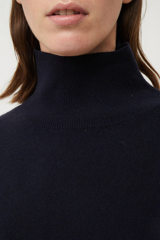 This image features the Kotto Sweater, highlighting its high-neck design and snug, comfortable fit. The sweater is presented in a classic, versatile ocean color, which enhances its elegant and timeless appeal.